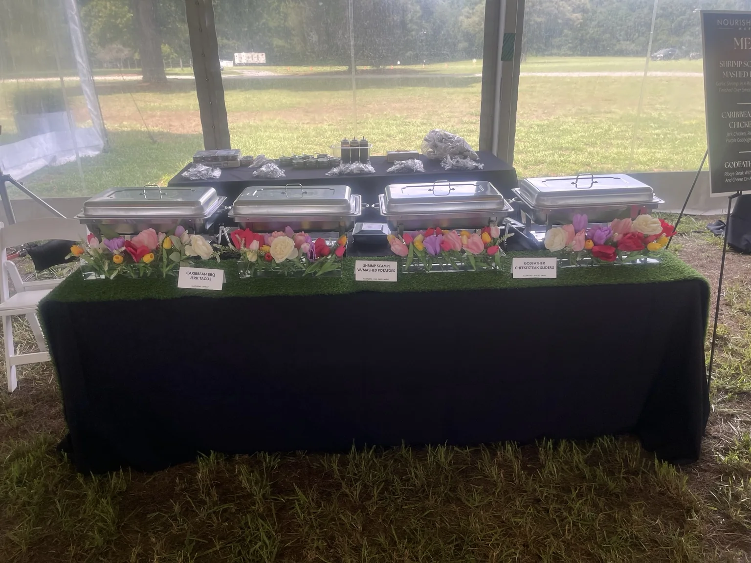 Wedding buffet station dressed in black with a green runner, colorful florals and covered chafing dishes.