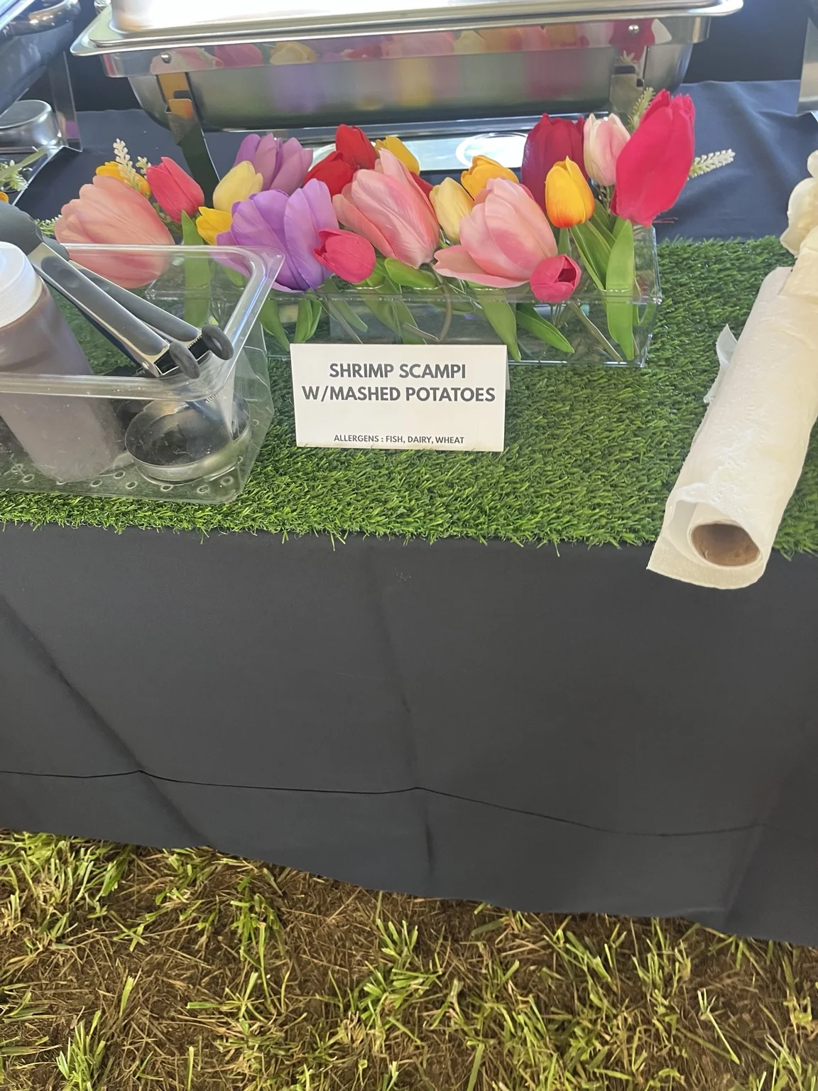 Colorful tulips arranged along a catering station beside a labeled shrimp scampi menu card.