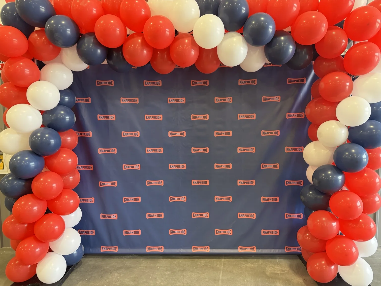 Knapheide step-and-repeat backdrop framed by a red, white and navy balloon installation.
