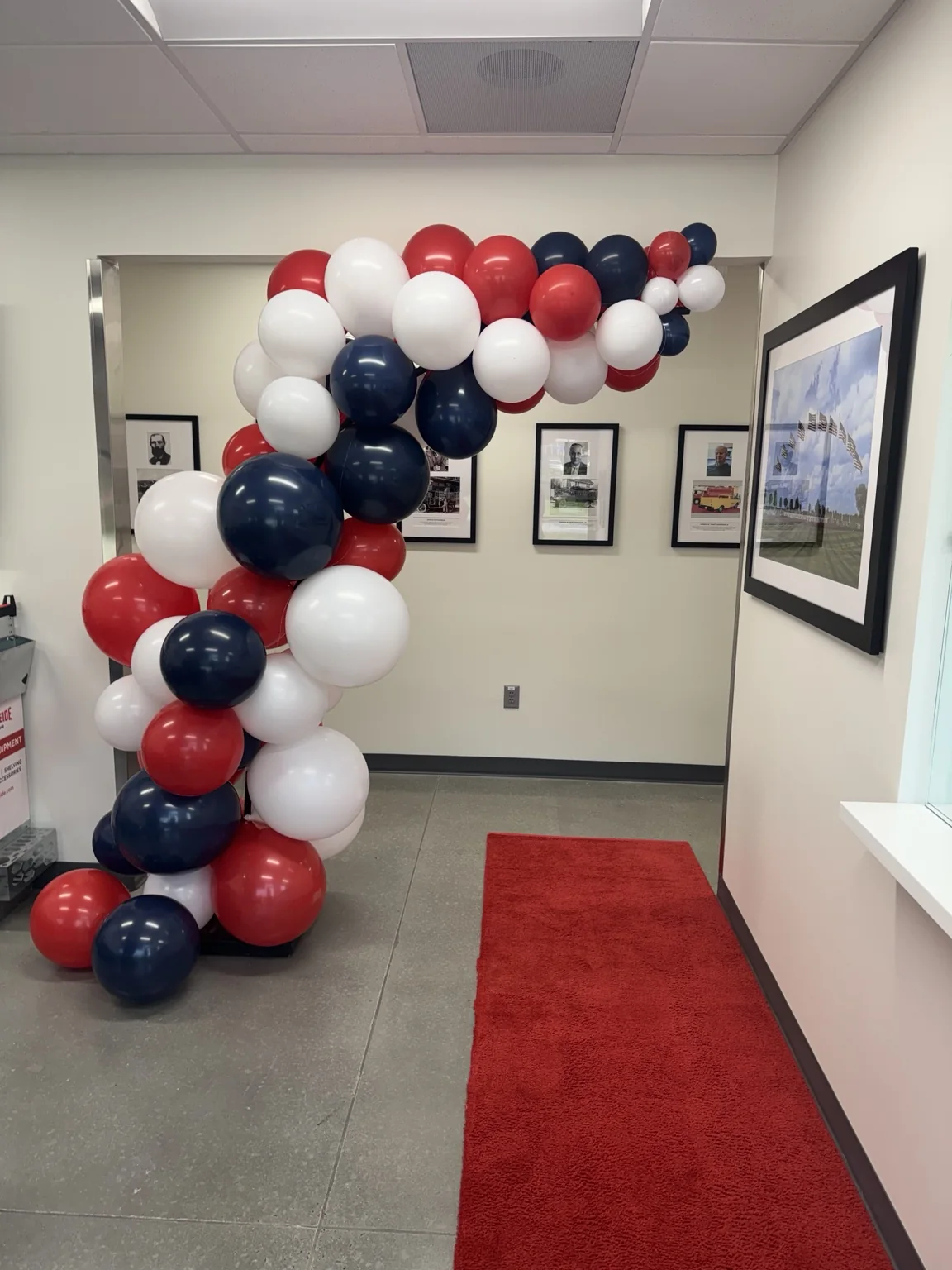 Red carpet entrance framed by a red, white and navy balloon installation at a corporate grand opening.