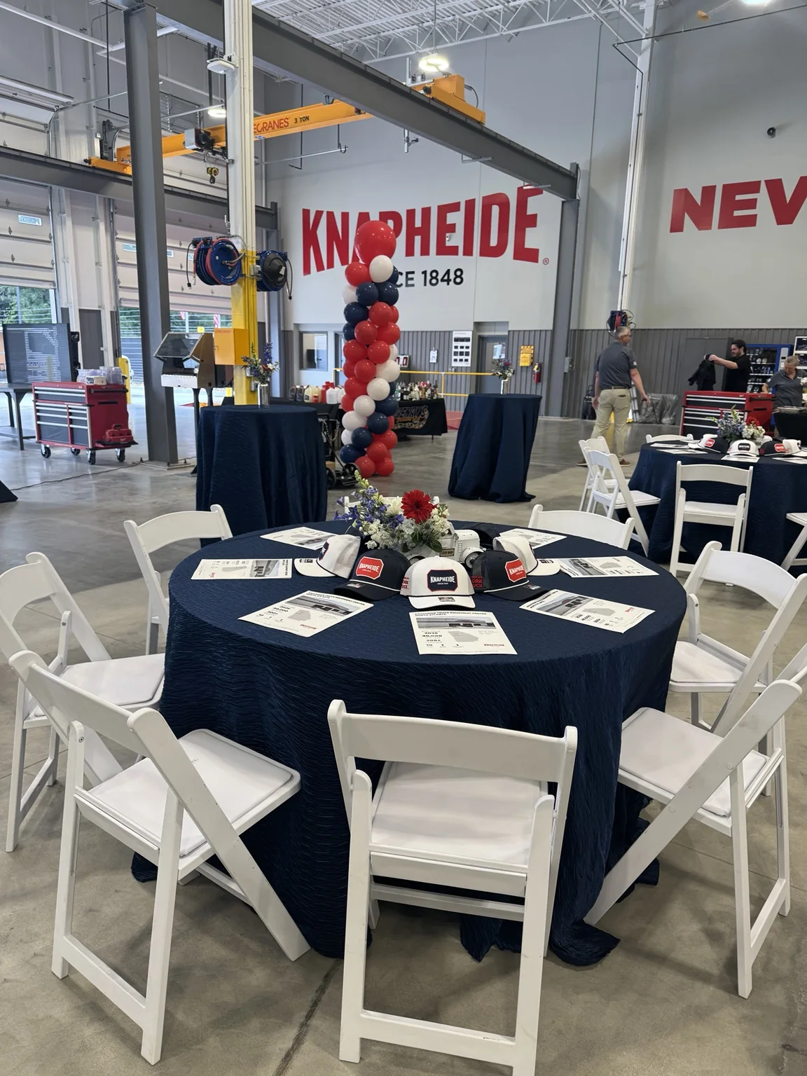 Branded corporate event table setting with navy linen, white chairs, floral centerpiece and Knapheide signage in the background.