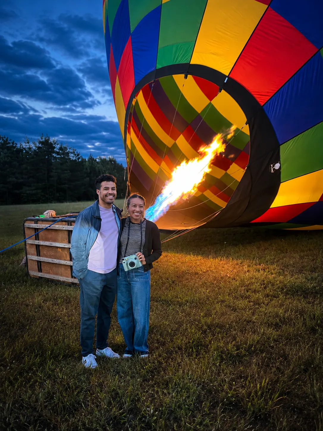 Guests standing beside a brightly colored hot-air balloon as its burner fires at dusk during the UnBridled program.